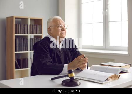 Juge sérieux et mûr assis à la réception avec livre de droit ouvert dans son bureau ou dans la salle d'audience Banque D'Images