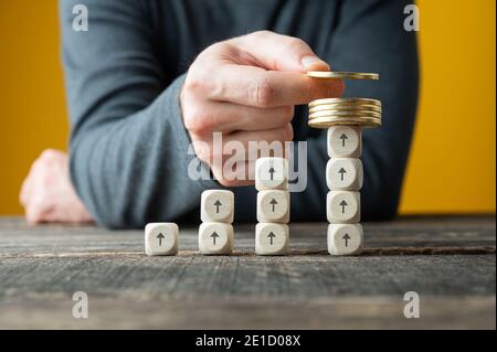 Image conceptuelle de l'investissement et du profit - main masculine plaçant des pièces d'or sur un graphique croissant présenté avec des blocs de bois. Banque D'Images