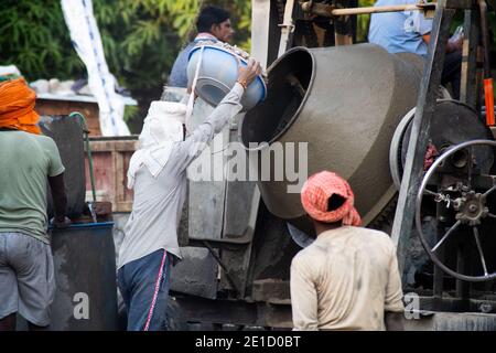 gros plan de travailleurs indiens de la construction sous-privegeed transportant du sable, du ciment, des pierres et de l'eau sur leur tête pour charger dans un mélangeur à faire Banque D'Images