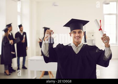 Diplômé avec un diplôme dans ses mains dans le bureau sur le fond de ses camarades de classe. Banque D'Images