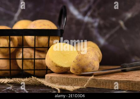 Couper les pommes de terre sur une planche à découper en bois avec des pommes de terre en métal panier en arrière-plan Banque D'Images