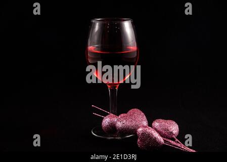 Verre à vin unique avec coeurs de Saint-Valentin sur fond noir. Banque D'Images