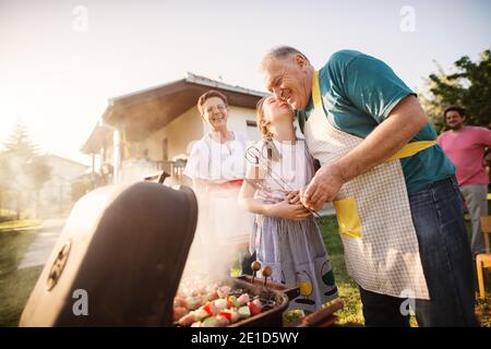 Les grands-parents fiers ont beaucoup de temps avec leur petite-fille, tout en faisant le barbecue dans l'arrière-cour. Banque D'Images