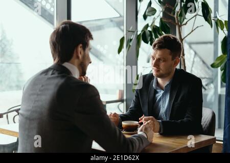 Deux hommes d'affaires parlent de nouvelles opportunités assis avec un ordinateur portable au bureau, projet de planification, considérant l'offre d'affaires, partager des idées Banque D'Images