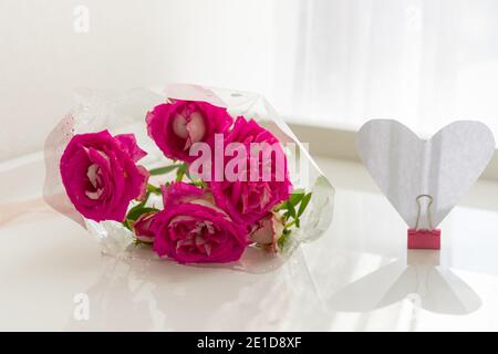 Roses sur la table et un coeur en papier. Composition pour la Saint-Valentin. Un bouquet de fleurs délicates dans un paquet avec un coeur créatif dans le soleil brillant Banque D'Images
