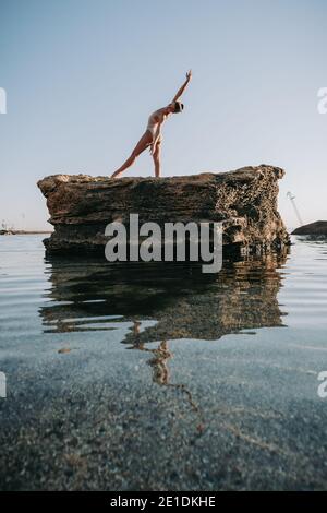 Ballerine jeune en maillot de bain beige danse ballet sur la mer ou la plage de sable de l'océan à la lumière du matin. Concept d'étirement, art, beauté de la nature. Banque D'Images