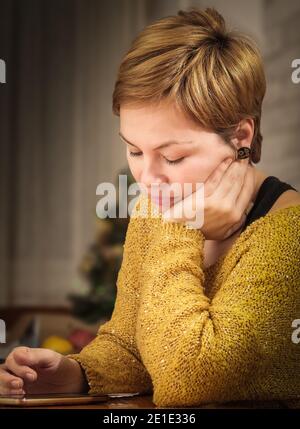 Jeune femme avec des cheveux courts, couleur miel, appréciant une soirée d'hiver détendue à la maison Banque D'Images