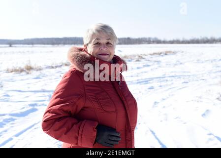 Portrait de la femme russe senior souriant sincèrement et regardant l'appareil photo contre un terrain enneigé. L'hiver Banque D'Images