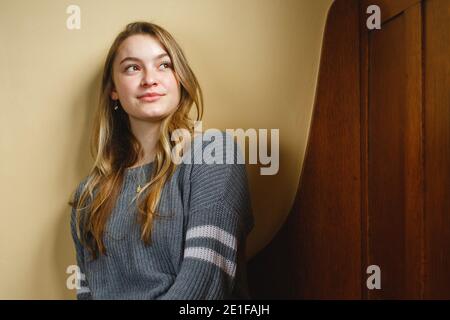 Une jeune femme est assise sur un banc en bois à l'intérieur, en regardant vers l'extérieur dans la distance Banque D'Images