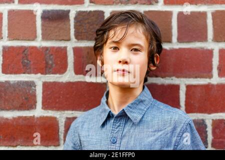 Un bel garçon sérieux penche sur le mur de brique avec un regard direct Banque D'Images