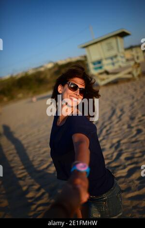 Heureuse femme caucasienne attirante tenant des photographes main, dansant et jouant sur la plage au coucher du soleil à Malibu, Californie Banque D'Images