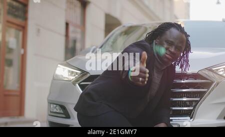 Homme d'affaires noir debout devant la nouvelle voiture et montrant le pouce vers le haut. Acheter une nouvelle voiture. Photo de haute qualité Banque D'Images