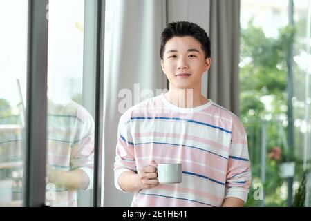 Bel homme, debout près de la fenêtre avec tasse de café du matin Banque D'Images