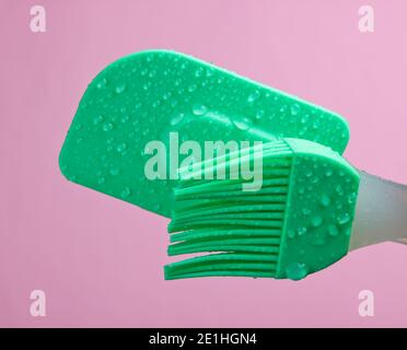 Brosse de cuisine en silicone et spatule pour cuire en gouttes de eau sur fond rose Banque D'Images