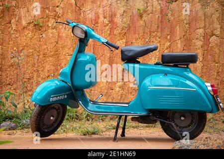 Vieille moto de scooter vintage exposée contre un mur d'argile. Couleur bleu clair et deux places, compartiments de rangement, phare rond à l'avant. Banque D'Images