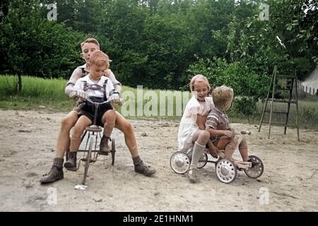 Kinder spielen mit und Rouleau Dreirad auf einem Spielplatz, Deutschland 1939. Les enfants avec des tricycles et scooters sur une aire de jeux, Allemagne 1939. Banque D'Images