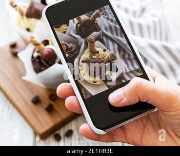 Fille fait une photo de cupcakes sur un smartphone Banque D'Images