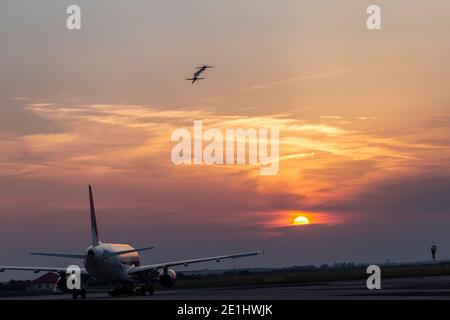 Deux petits avions faisant des acrobaties au coucher du soleil et un avion de ligne attendant sur le runaway à décollage. Spectacle aérien de Timisoara ou événement Aerotim le 15 de Banque D'Images