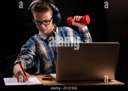 jeune étudiant avec deux haltères devant l'ordinateur portable à l'école à domicile Banque D'Images