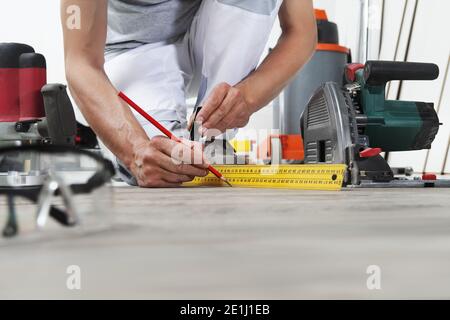 homme main de travail d'installation de plancher stratifié de bois, prend la mesure avec le carré d'acier de menuisier et le crayon. Rénovation de maisons en parquet. Banque D'Images