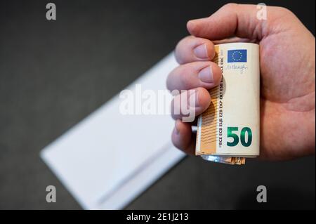 Un chèque de paie blanc a été ouvert sur une table noire : la main contient un rouleau volumineux de 50 billets en euros. Image conceptuelle de salaire. Banque D'Images