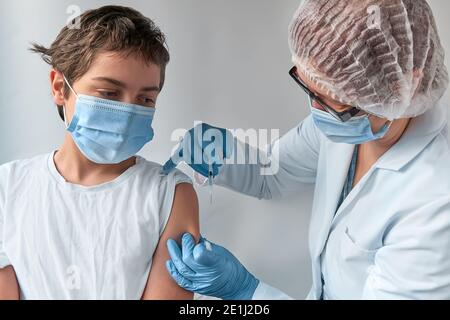 Gros plan sur les mains dans des gants avec une seringue et l'épaule du patient, enfant de l'adolescence. Covid 19, concept de vaccin contre la grippe, le tétanos ou la rougeole. Medic, médecin ou Banque D'Images