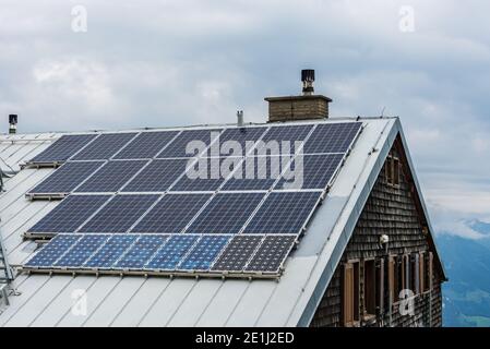 Panneaux photovoltaïques solaires PV sur le toit d'une maison. L'électricité du soleil pendant l'hiver. Maison avec fenêtres et cheminée, montagnes à l'arrière-plan. Banque D'Images