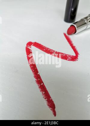 Frottis de rouge à lèvres éclatant avec de minuscules particules de microplastique sur un fond en bois blanc Banque D'Images