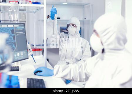 Femme scientifique en coverall utilisant une micropipette en laboratoire pour la recherche sur le coronavirus. Équipe de microbiologistes en laboratoire de recherche menant des expériences pendant une pandémie mondiale avec le covid19. Banque D'Images