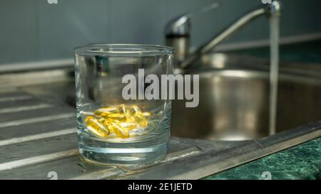 Un pot en verre tenu à la main avec des capsules de couleur or jaune - compléments alimentaires, vitamines, médecine Banque D'Images