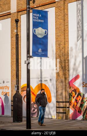 Uxbridge, Royaume-Uni. 7 janvier 2021. Un homme portant un masque facial sous une bannière demandant à être porté à Uxbridge, dans le nord-ouest de Londres, le matin où le troisième verrouillage national est entré en vigueur. Le gouvernement britannique a imposé des restrictions plus sévères pour lutter contre une souche variante récemment découverte, le nombre de décès et de cas de coronavirus liés à Covid-19 continuant d'augmenter. Boris Johnson, premier ministre, est député de la circonscription d'Uxbridge et de South Ruislip. Credit: Stephen Chung / Alamy Live News Banque D'Images