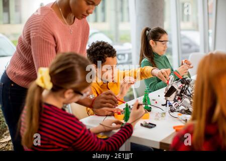 Femme afro-américaine smily enseignant en sciences avec un groupe d'enfants programmation de jouets électriques et de robots dans les salles de classe de robotique Banque D'Images