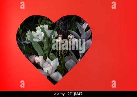 Trou dans le papier rouge en forme de coeur à travers avec des fleurs et des feuilles sont visibles. Concept de bonne Saint Valentin Banque D'Images