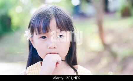 Mignon petite fille asiatique Tuck une fleur blanche dans son et regardez l'appareil photo Banque D'Images