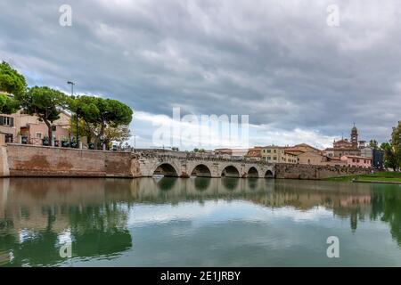 L'ancien pont d'Auguste et de Tiberius se reflète dans l'eau du canal dans le centre historique de Rimini, en Italie, par une journée nuageux Banque D'Images