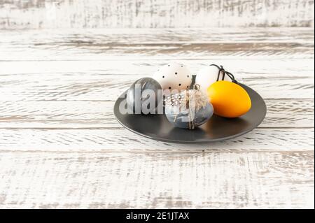 Œufs de pâques tendance de couleur foncée et plumes sur une assiette sur une table en bois. Préparation pour les vacances de pâques. Composition fesstive Banque D'Images