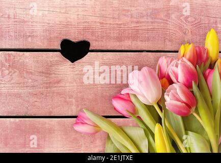 Bouquet de printemps brillant de tulipes colorées sur fond de bois avec un trou en forme de coeur. Carte de vœux pour la Saint-Valentin, mère. Ressort h Banque D'Images