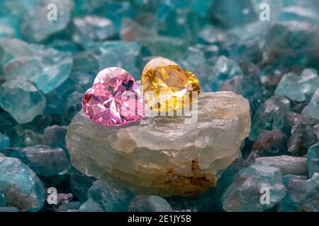 les diamants en forme de coeur jaune et rose sont placés ensemble sur des pierres précieuses brutes bleu ciel. Banque D'Images