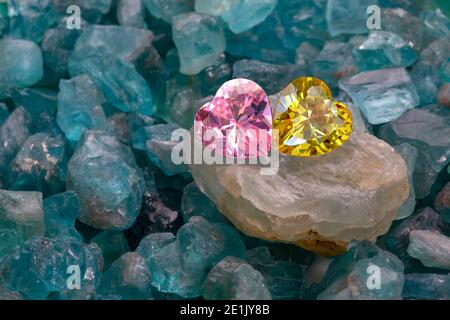les diamants en forme de coeur jaune et rose sont placés ensemble sur des pierres précieuses brutes bleu ciel. Banque D'Images
