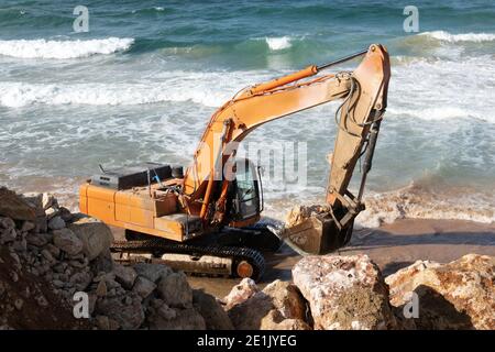 La pelle hydraulique jaune travaille sur la plage de mer avec des vagues sur le fond à tel Aviv, Israël Banque D'Images