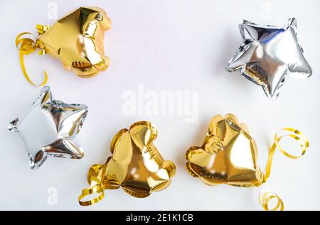 Trois coeurs dorés et des ballons d'aluminium aux étoiles, vue de dessus sur un fond blanc. Saint-Valentin, carte postale. Banque D'Images