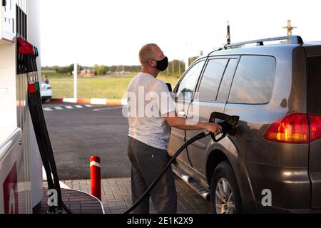 homme dans un masque de protection noir ravitailler une voiture à une station-service, protection contre les virus, foyer sélectif Banque D'Images