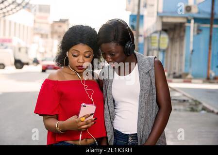 Deux jeunes femmes belles et heureuses sont souriantes, parlent et recherchent quelque chose sur un téléphone cellulaire dans la ville Banque D'Images