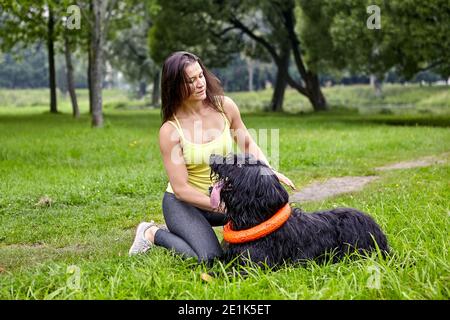 Le chien noir briard couché sur l'herbe et regarde sa femme propriétaire, qui est assise à proximité. Banque D'Images