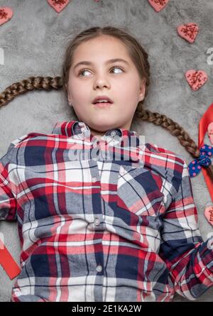 Portrait d'une jolie fille souriante et charmante avec des picots amusants sur un tapis gris avec des biscuits doux au coeur. Concept de Saint-Valentin ou d'anniversaire Banque D'Images