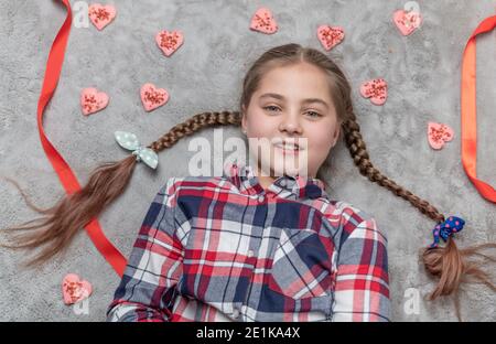 Portrait d'une jolie fille souriante et charmante avec des picots amusants sur un tapis gris avec des biscuits doux au coeur. Concept de Saint-Valentin ou d'anniversaire Banque D'Images