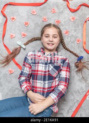 Portrait d'une jolie fille souriante et charmante avec des picots amusants sur un tapis gris avec des biscuits doux au coeur. Concept de Saint-Valentin ou d'anniversaire Banque D'Images