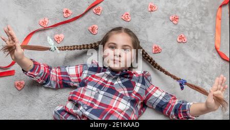 Portrait d'une jolie fille souriante et charmante avec des picots amusants sur un tapis gris avec des biscuits doux au coeur. Concept de Saint-Valentin ou d'anniversaire Banque D'Images