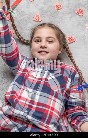 Portrait d'une jolie fille souriante et charmante avec des picots amusants sur un tapis gris avec des biscuits doux au coeur. Concept de Saint-Valentin ou d'anniversaire Banque D'Images