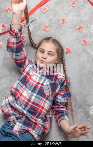 Portrait d'une jolie fille souriante et charmante avec des picots amusants sur un tapis gris avec des biscuits doux au coeur. Concept de Saint-Valentin ou d'anniversaire Banque D'Images